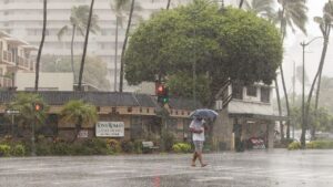 A person with an umbrella crossing a rainy street near a railway crossing.