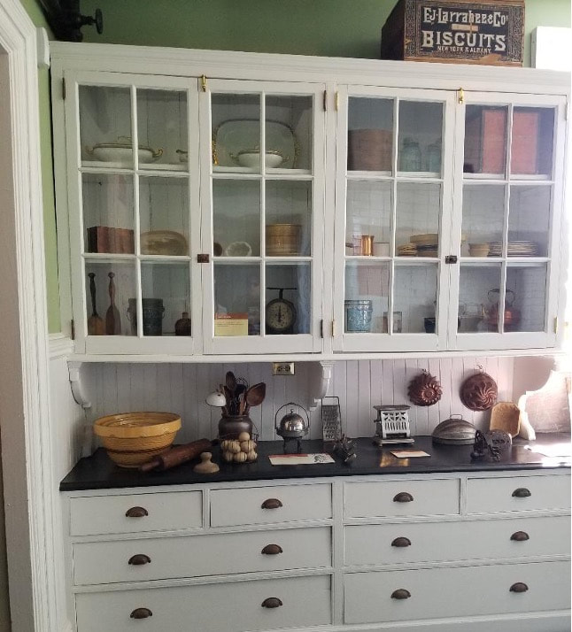 White kitchen cabinet with glass doors displaying dishes and bowls.