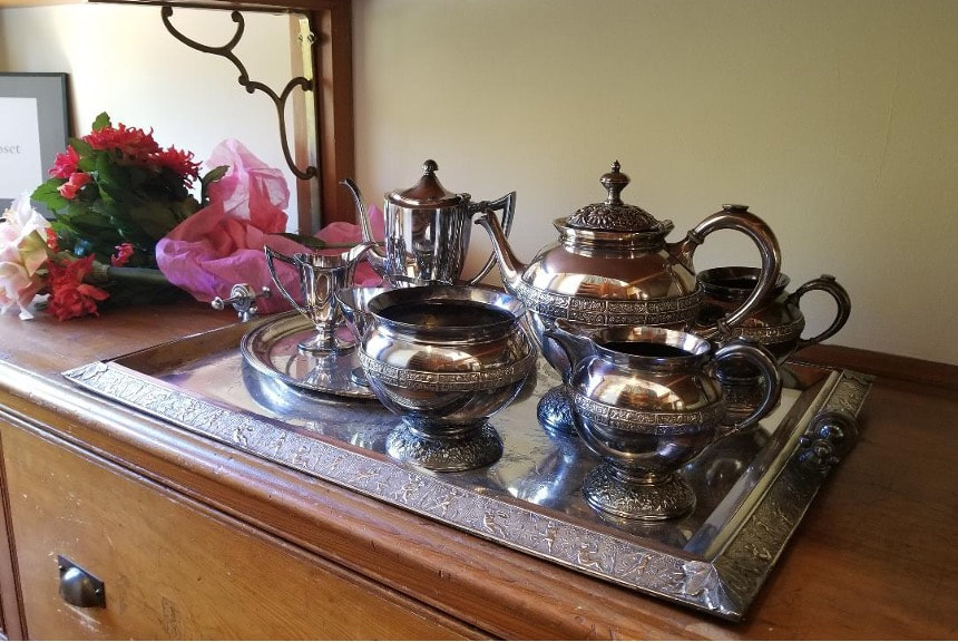 Elegant vintage silver tea set on a tray with pink flowers in the background.