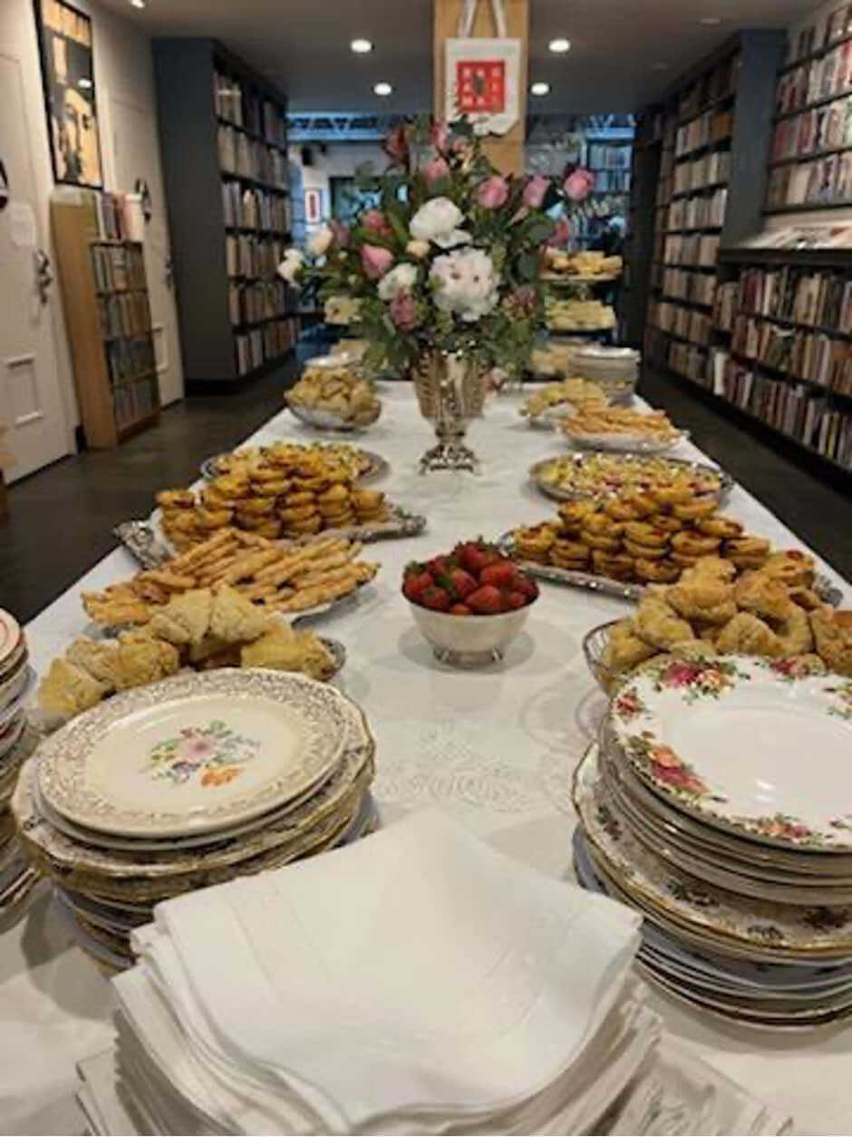 Elegant buffet setup with pastries and fresh flowers in a cozy bookshop.