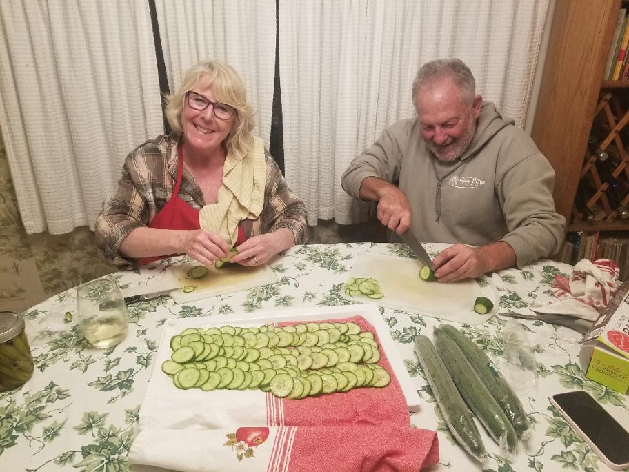Two elderly people preparing sliced cucumbers at a table.