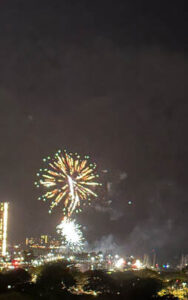 Colorful fireworks burst in the night sky over a city.