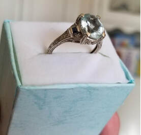 Elegant silver ring with a large clear gemstone in a light blue velvet box.