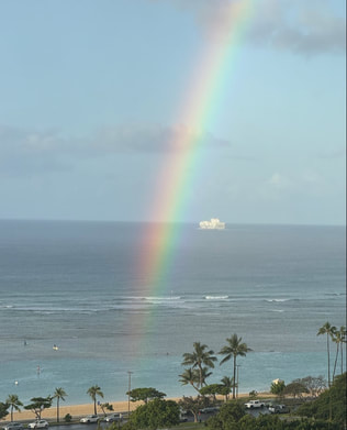 A vibrant rainbow arches over the ocean with a ship on the horizon.