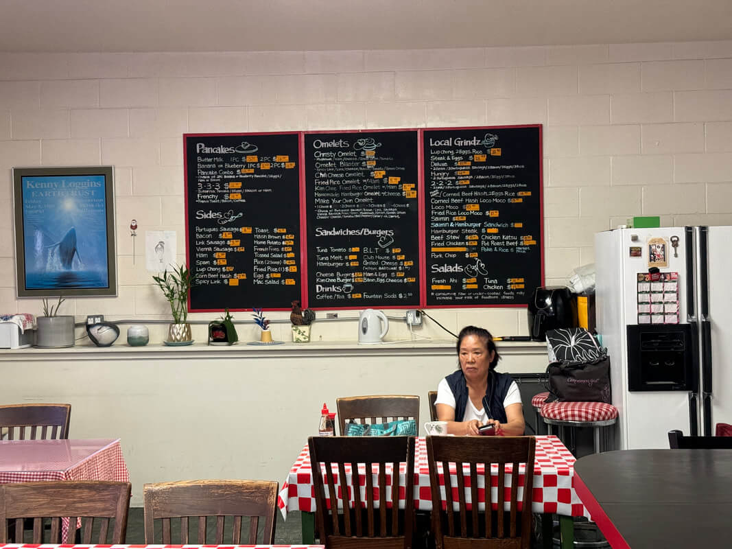 Woman sitting at a table in a cozy cafe with a menu board behind her.