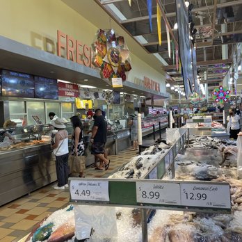 People shop in a busy grocery store aisle with fresh seafood on display.