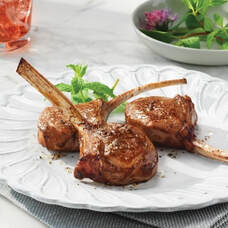 Grilled lamb chops seasoned and served on a white plate with herbs.