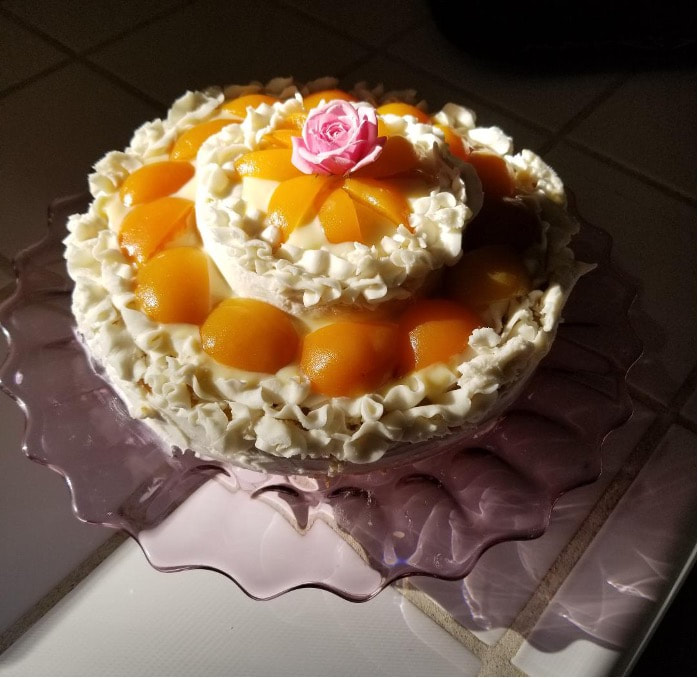 A peach and cream decorated cake with a pink rose on top.