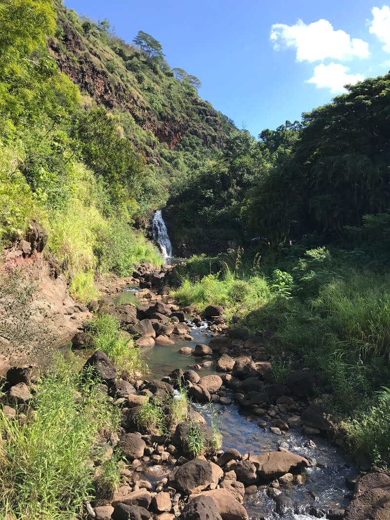 Person exploring a rocky stream in a lush green valley.