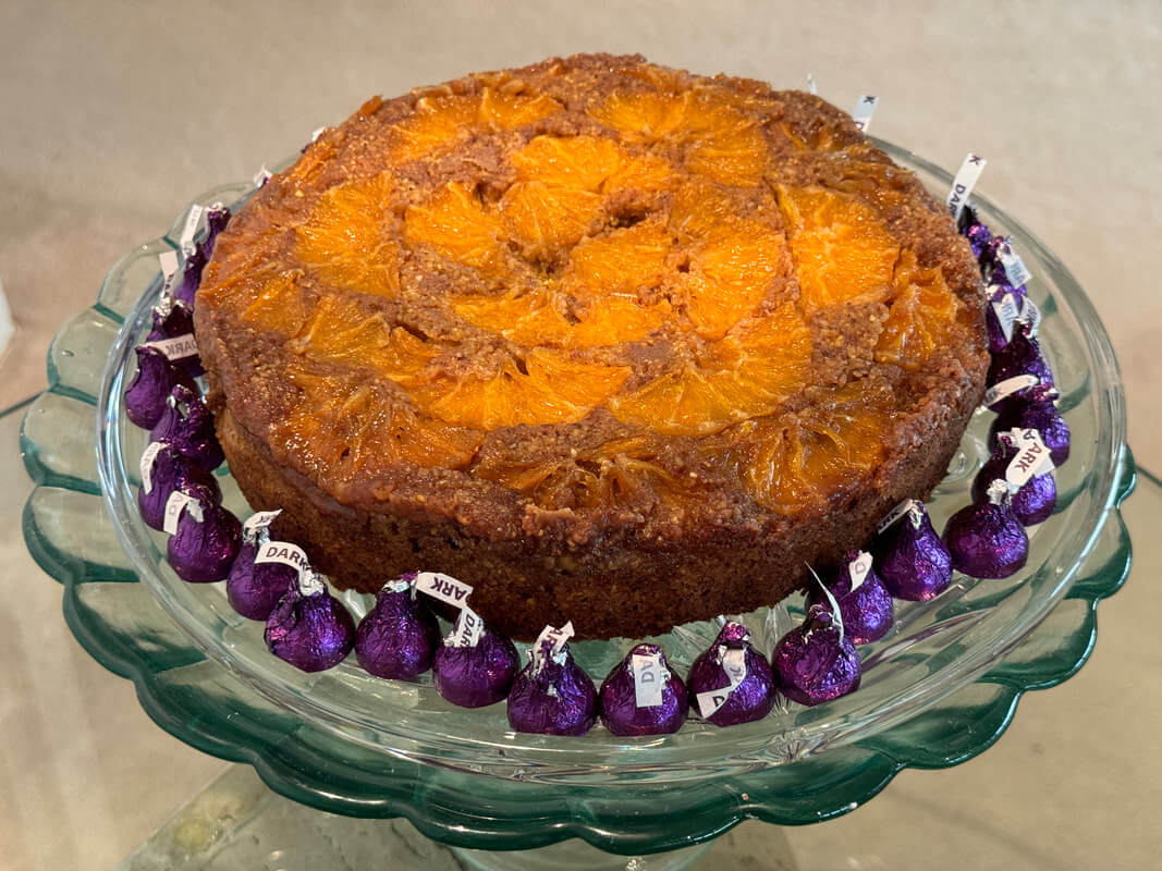 A homemade bundt cake decorated with purple and white flowers on a glass plate.