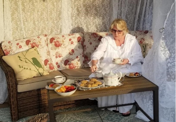 Woman in white robe enjoying tea and snacks on a floral sofa.