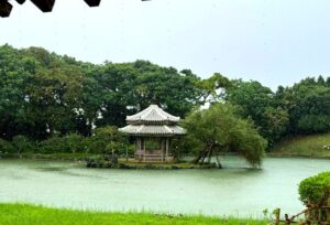 A serene gazebo on an island in a pond surrounded by greenery.