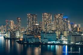 Night view of a city skyline with illuminated high-rise buildings reflecting on water.