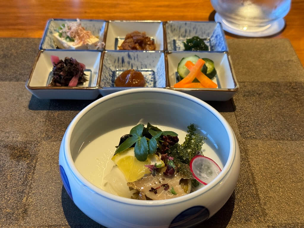 A bowl of creamy soup with herbs and a side of assorted vegetables and condiments.