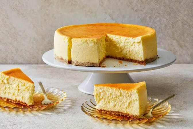 Classic creamy cheesecake with a golden top and a slice served on a plate.