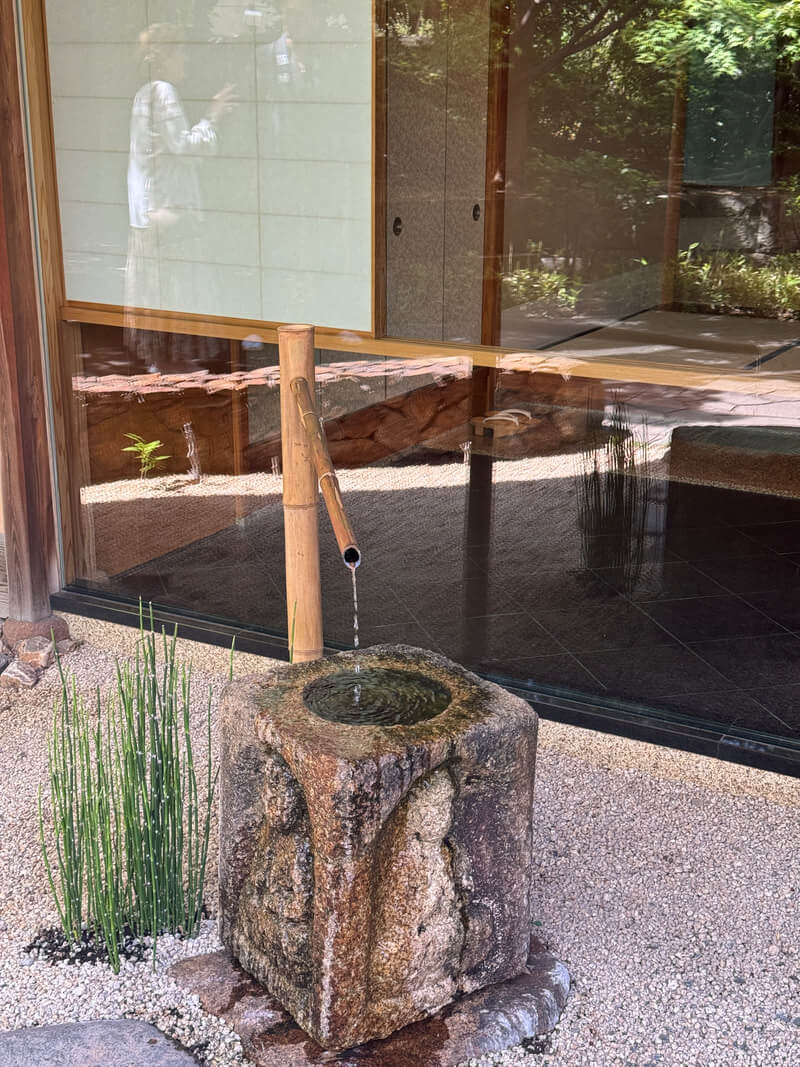 A traditional bamboo water fountain flowing into a hollowed tree stump basin.