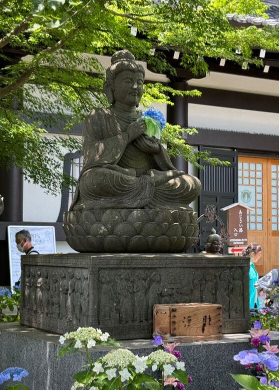 Statue of a child sitting on a lotus flower with greenery and building in background.
