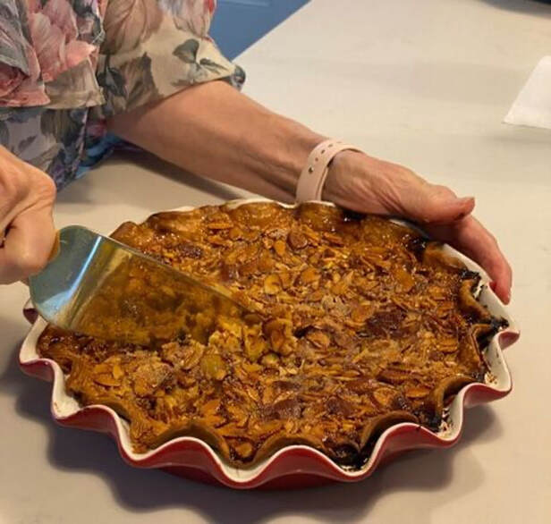 A person slicing a freshly baked pecan pie in a red scalloped dish.