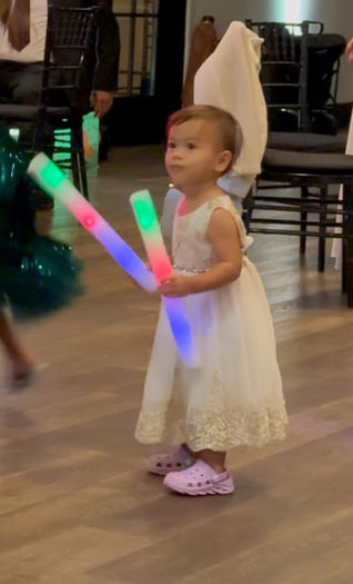 A toddler in a white dress holding colorful light sticks.
