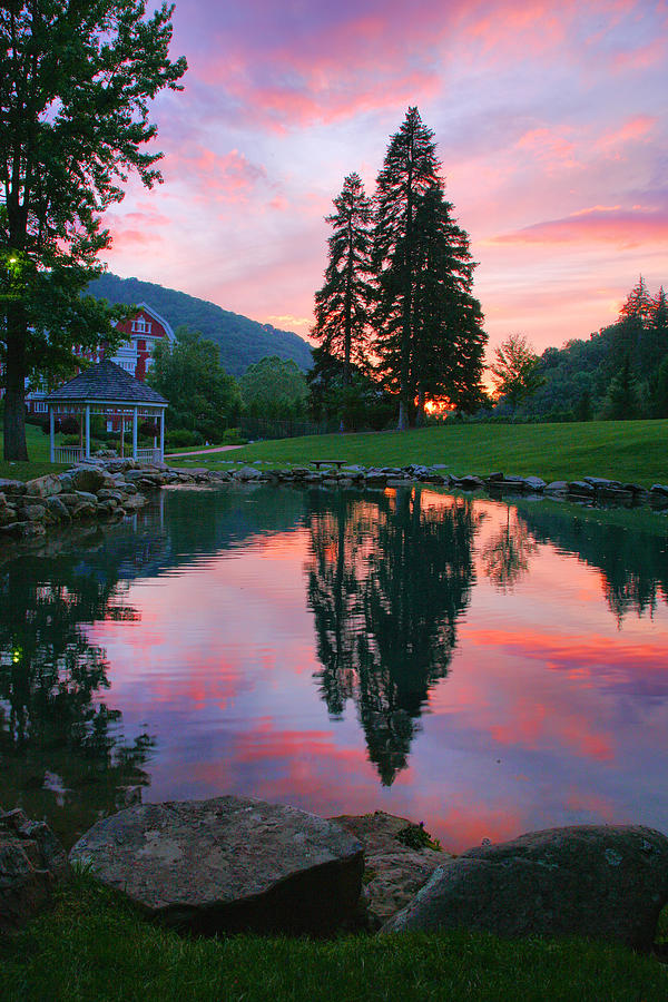 Sunset reflecting on a serene mountain lake with tall trees.