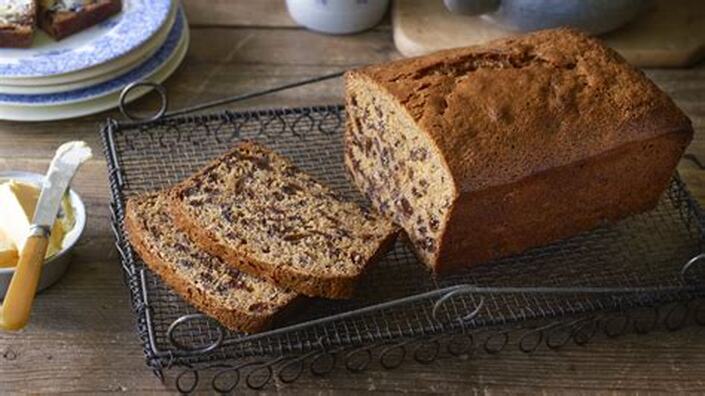 Loaf of nut bread with two slices on a wire rack.
