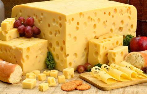 Assorted cheese blocks with grapes and crackers on a white surface.
