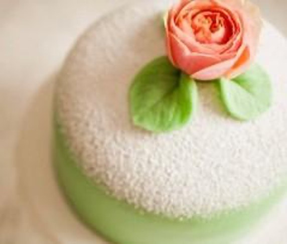 Elegant white cake with a pink rose and green leaves decoration.