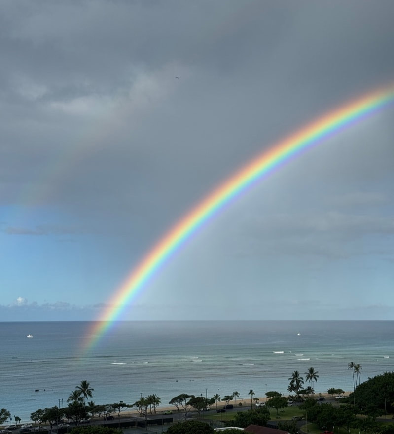A vibrant rainbow stretches over the ocean under a cloudy sky.