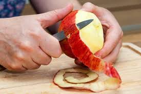 Hands peeling a red apple with a knife.