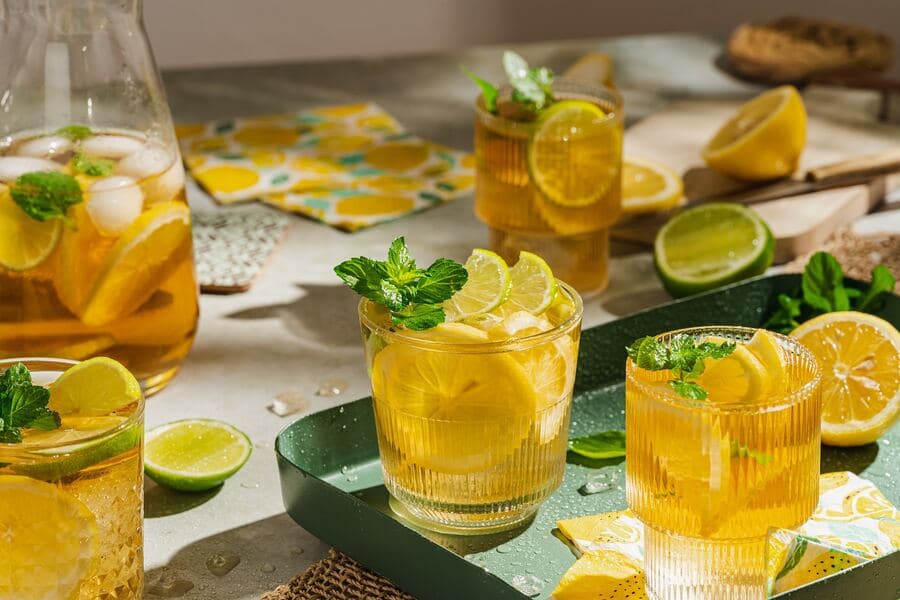 Refreshing iced lemon tea with mint and lime slices on a green tray.