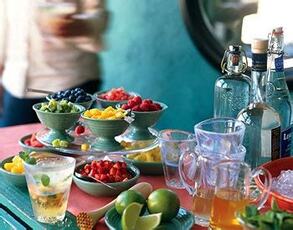 A colorful display of fresh fruits and drinks on a table with a blurry person in the background.