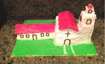 A handcrafted model of a church with a red roof and white walls.