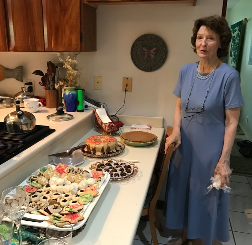 A woman in a blue dress stands by a kitchen counter with various dishes.