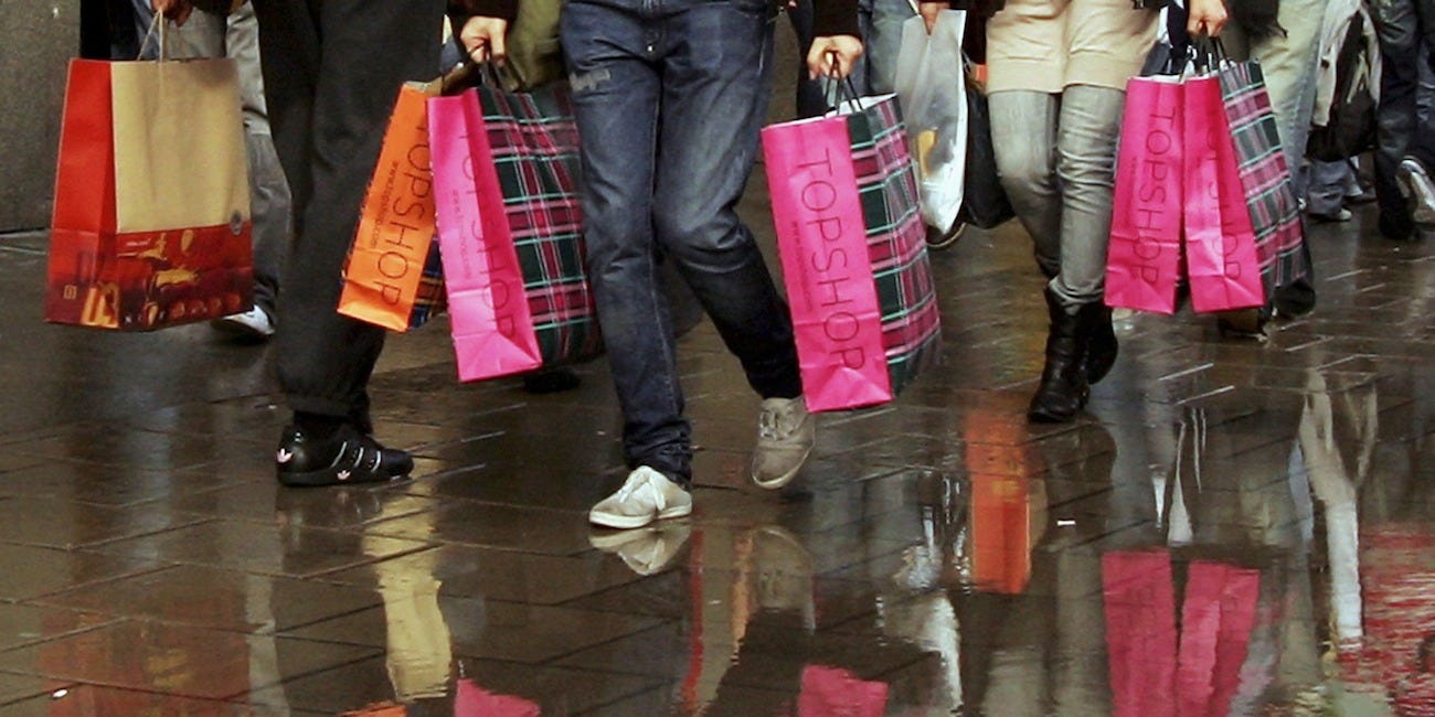 People walking with colorful shopping bags on a wet pavement.
