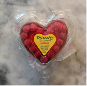 Heart-shaped container of Driscoll's raspberries on marble surface.
