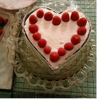 Heart-shaped cake decorated with raspberries on a glass plate.