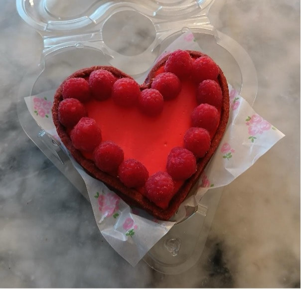 Heart-shaped dessert topped with red macarons on glass plate.