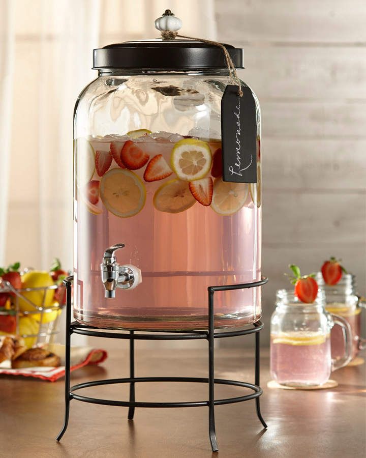 Glass dispenser with pink lemonade and fruit slices on metal stand.