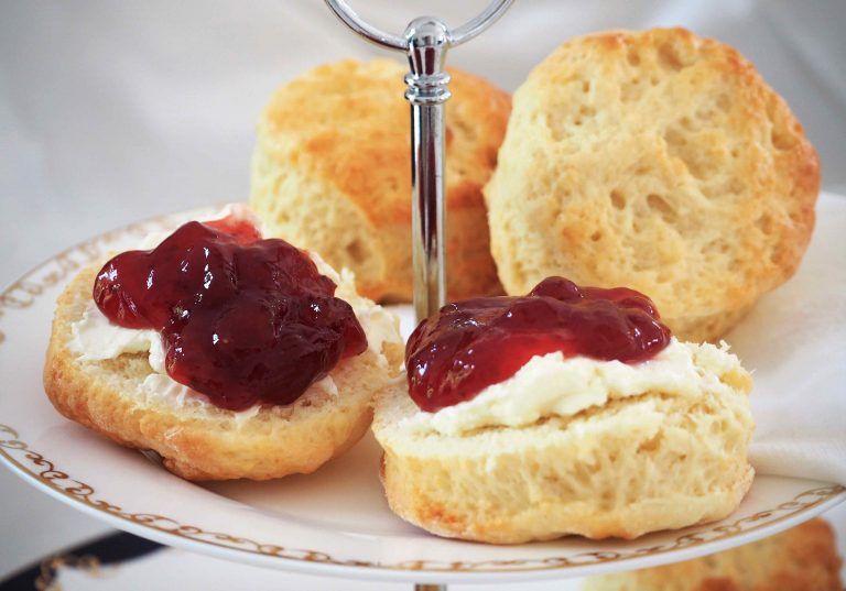 Scones topped with clotted cream and strawberry jam on a plate.