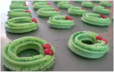 Green piped frosting shapes with red sugar beads on a baking tray.