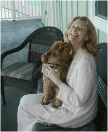 Woman in pink robe happily holding a small brown dog.