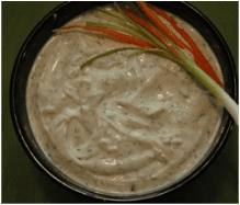 A bowl of creamy herb dip garnished with carrot and celery sticks.