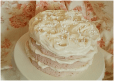 A layered pink and white cake decorated with white icing and pearl sprinkles.
