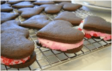 Heart-shaped chocolate cookies with pink cream filling on a cooling rack.