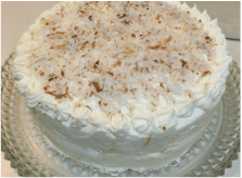 A round cake with white frosting and toasted coconut flakes on top.