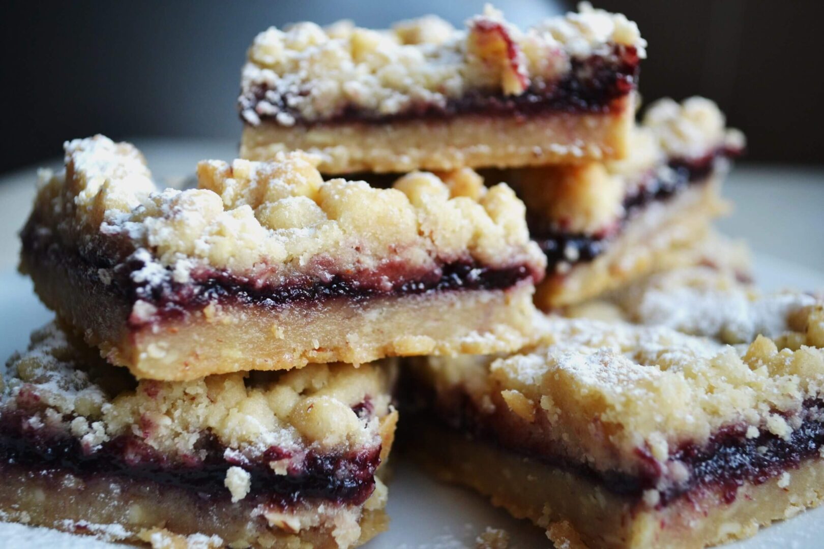 Close-up of crumbly jam-filled bars stacked on a plate.