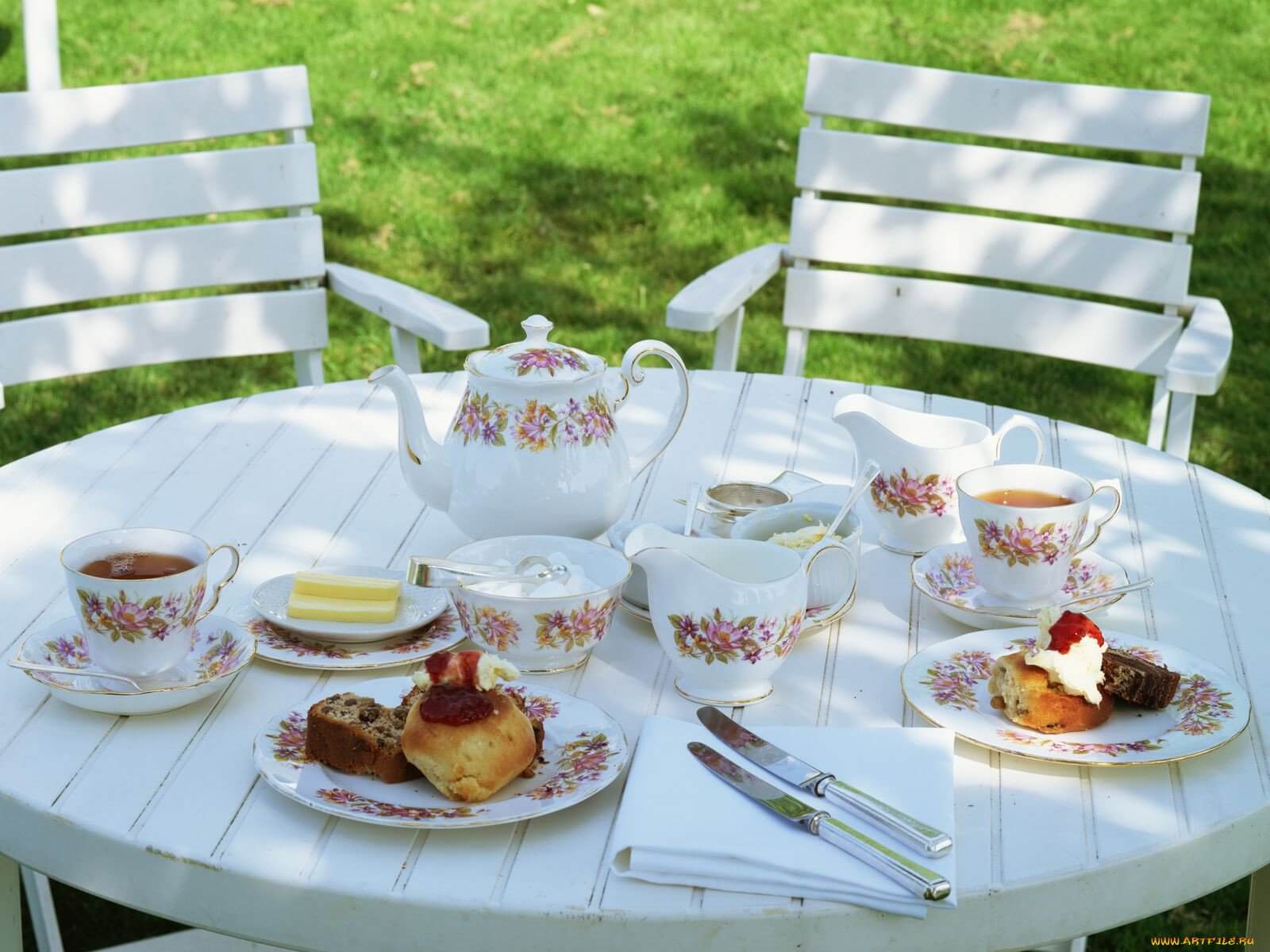 Outdoor tea party setup with scones, cream, and jam on a white table.