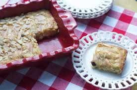 A slice of nut-topped pastry on a plate next to a red baking dish.