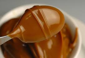 Close-up of creamy caramel sauce dripping from a spoon.
