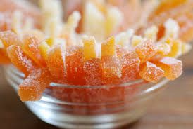 Close-up of sugar-coated orange candy sticks in a glass bowl.